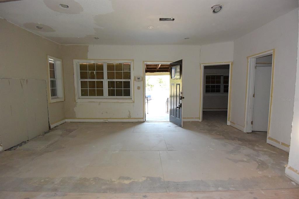 An unfinished room with bare drywall, exposed subflooring, and an open front door — 913 E 28TH AVENUE, TAMPA, FL
