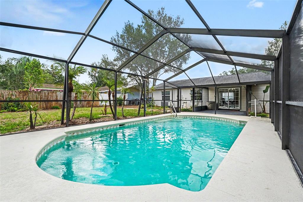 A swimming pool with a screen enclosure sits in the backyard of a single-story house — 2022 LANCE COURT, DOVER, FL