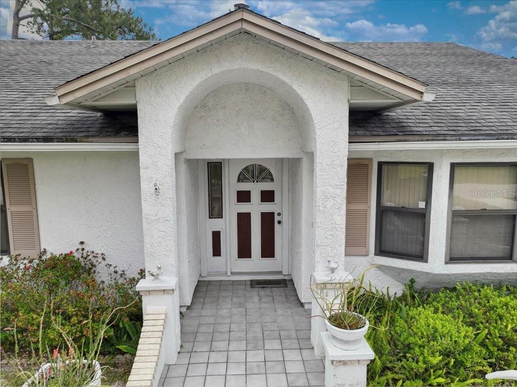 The exterior of a house features a white stucco facade, an arched entryway, and a tiled porch — 20 FORSYTHE LANE, PALM COAST, FL