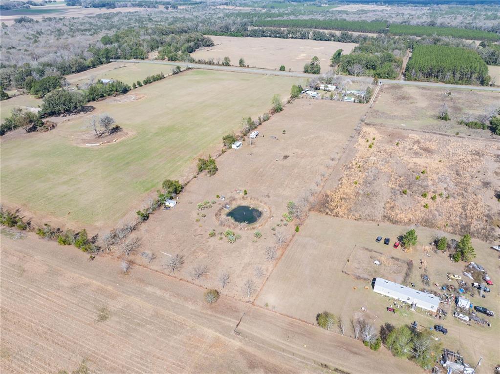 An aerial view shows a large, open rural property featuring a small pond and several structures — 3378 W STATE ROAD 238, LAKE BUTLER, FL