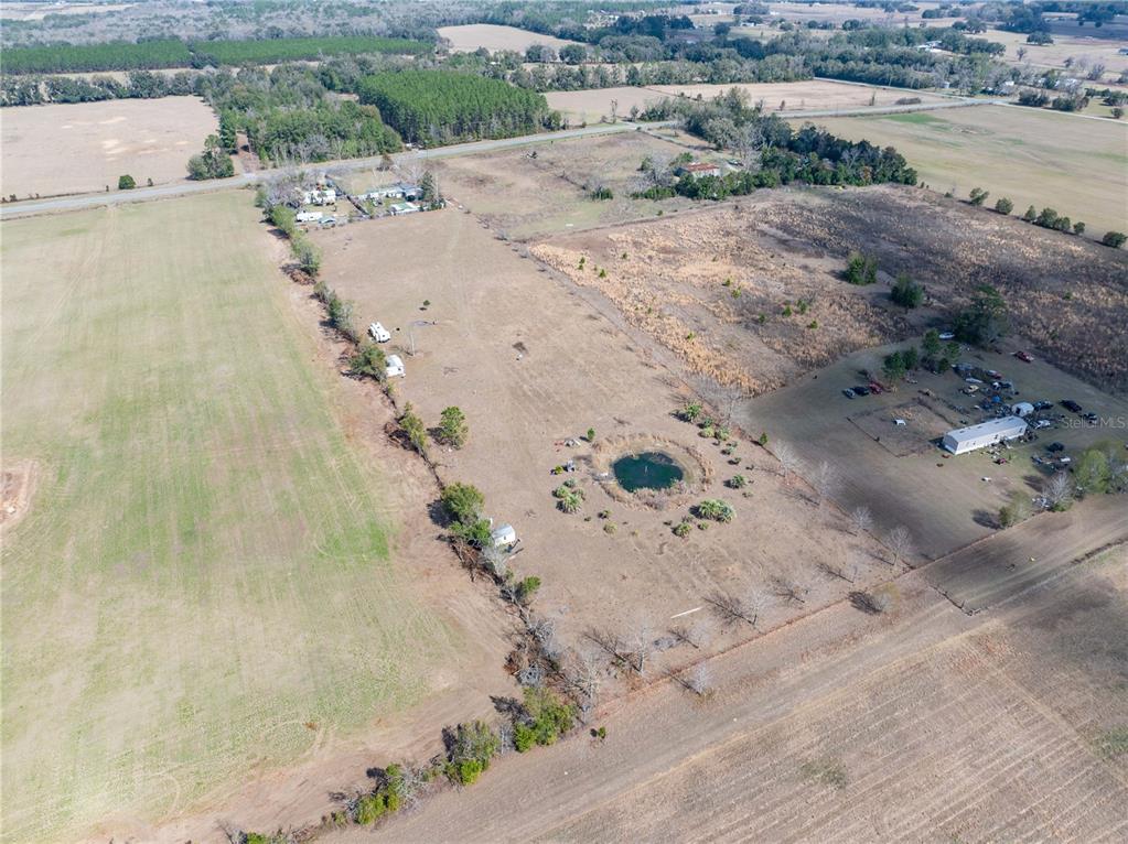 An aerial view shows a large, open rural property featuring a small pond and structures — 3378 W STATE ROAD 238, LAKE BUTLER, FL