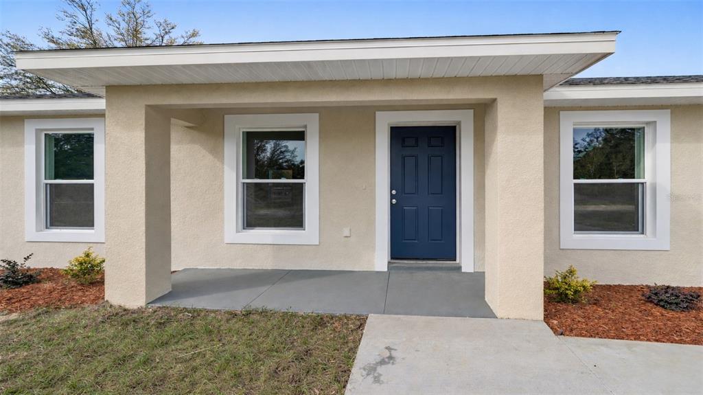 A beige house exterior features a blue front door, a white garage, and a concrete porch — 24763 NW HIGHVIEW AVENUE, DUNNELLON, FL