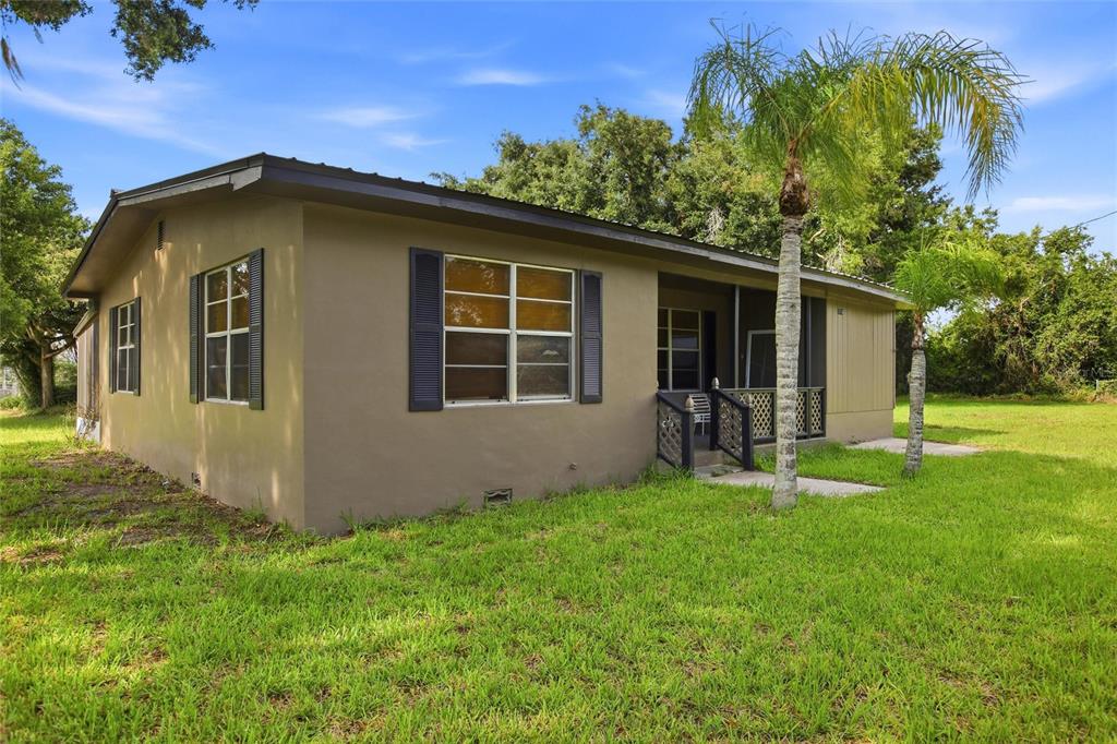 A single-story house with tan stucco walls, dark shutters, and a screened-in front porch — 2616 HACIENDA DRIVE, LORIDA, FL