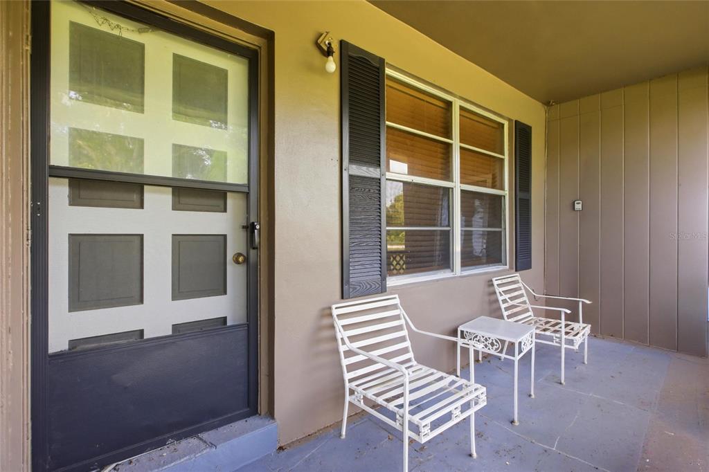 A covered porch features a screen door, a window with black shutters, and white metal furniture — 2616 HACIENDA DRIVE, LORIDA, FL