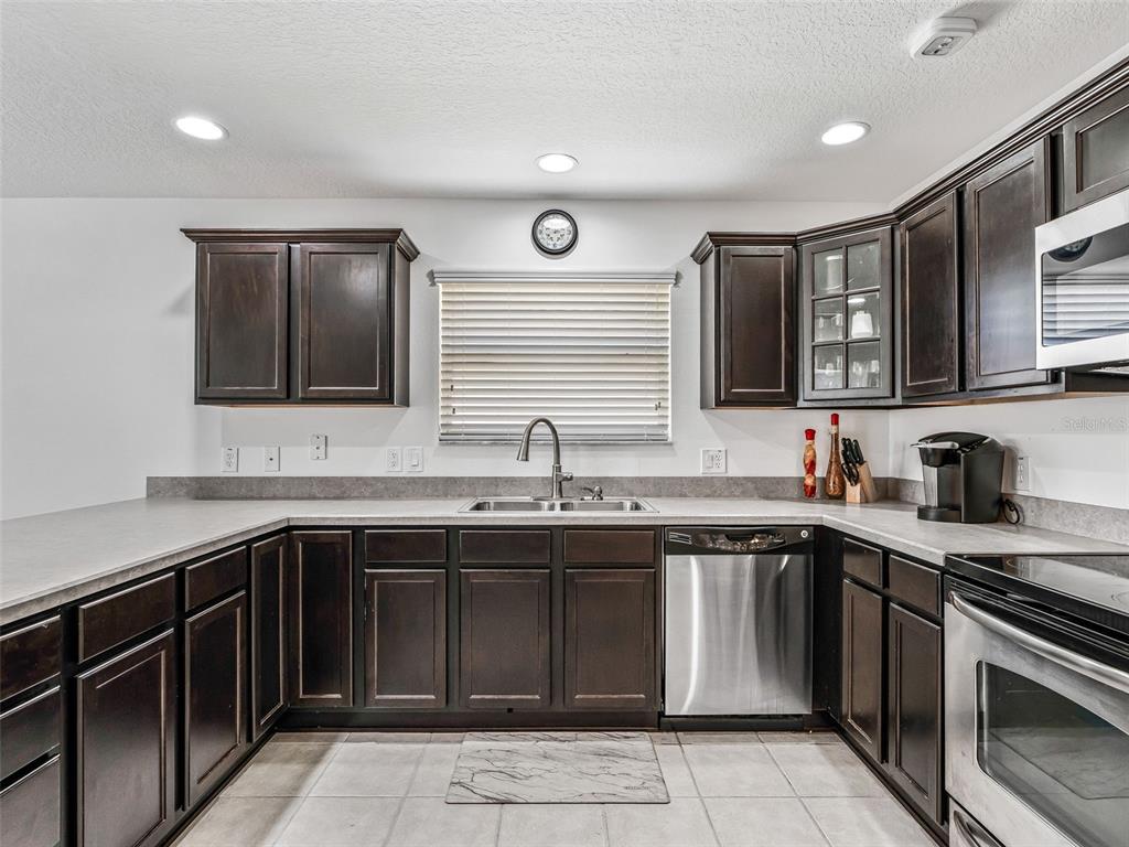 A kitchen features dark wood cabinets, stainless steel appliances, and light-colored countertops — 764 BAISLEY TRAIL, THE VILLAGES, FL