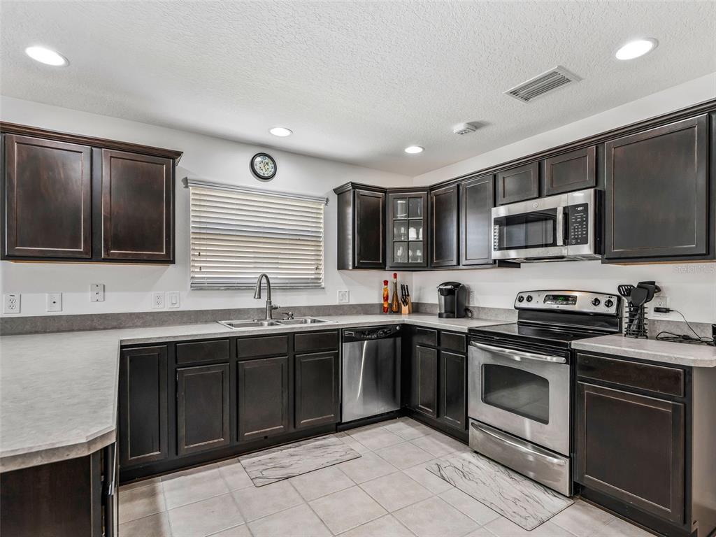 A kitchen features dark wood cabinets, stainless steel appliances, and light-colored countertops — 764 BAISLEY TRAIL, THE VILLAGES, FL