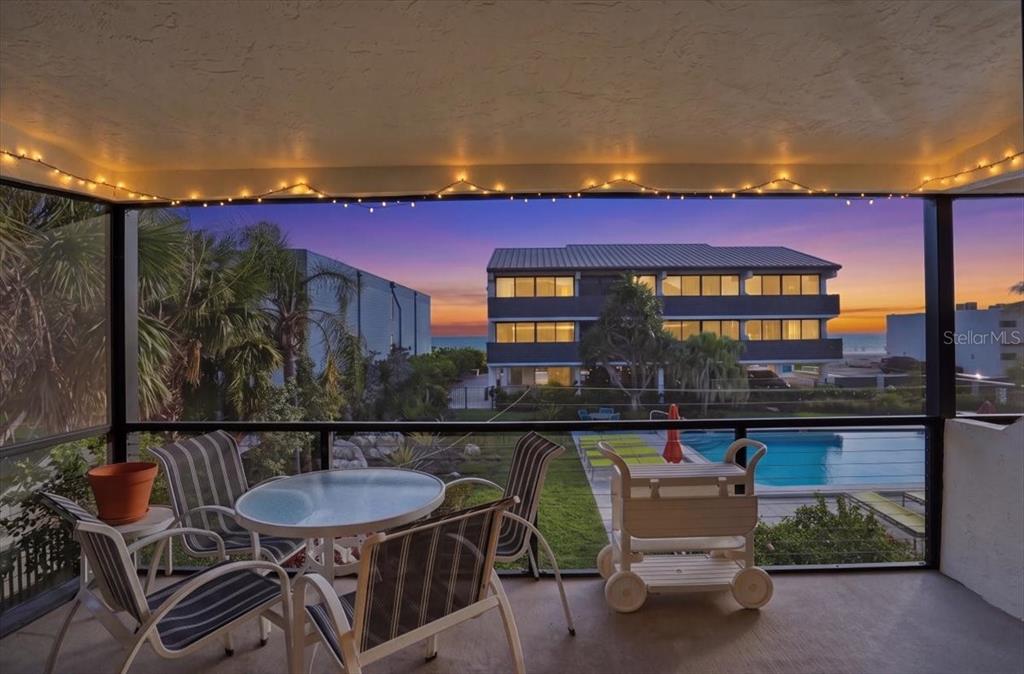 A screened-in balcony overlooks a swimming pool and a multi-story building at sunset — 6804 GULF DRIVE UNIT 6804, HOLMES BEACH, FL