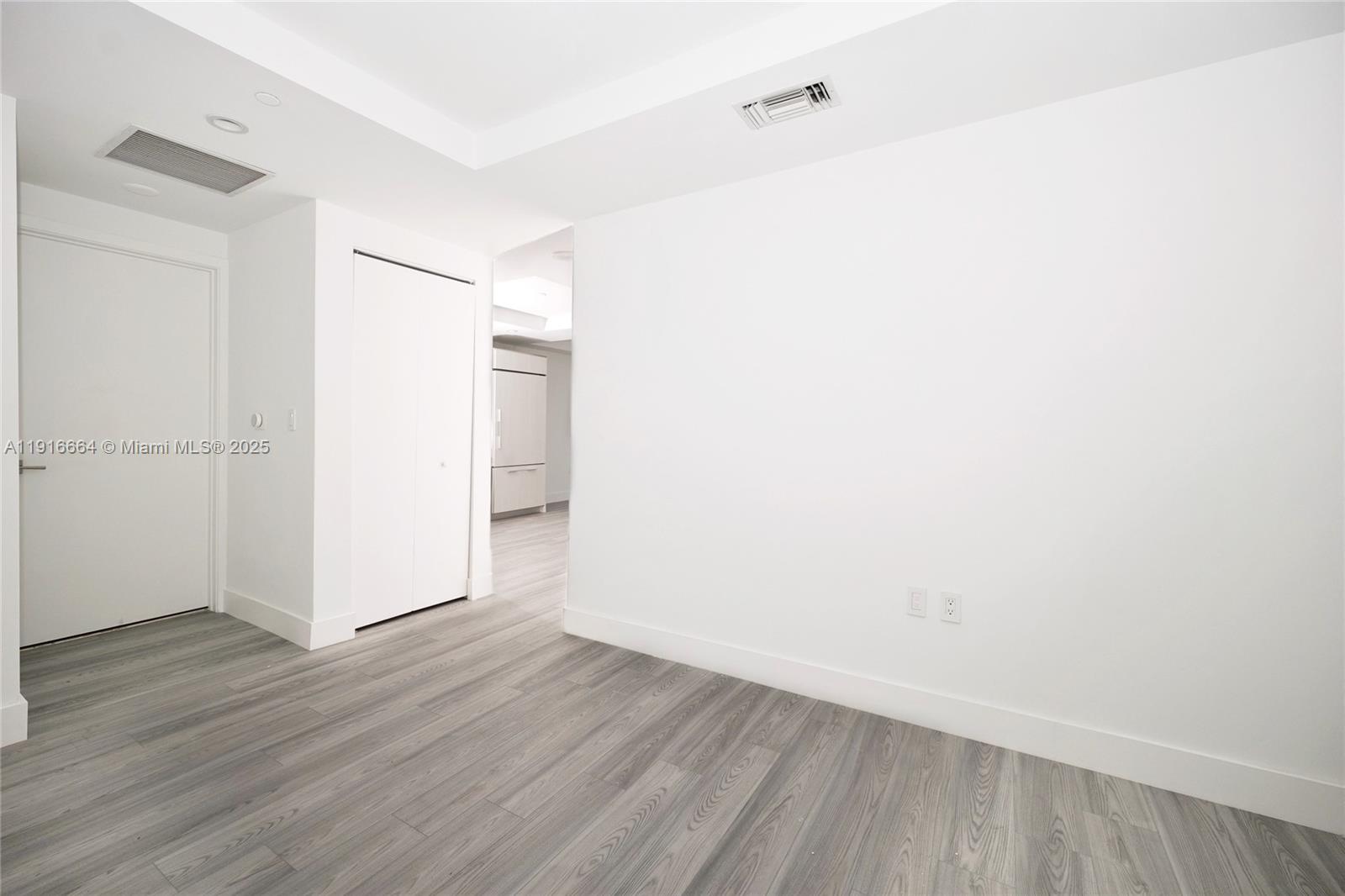 A minimalist room features white walls, light gray wood-look flooring, and a closed closet door — 45 SW 9th St # 1504, Miami FL 33130, MIAMI, FL