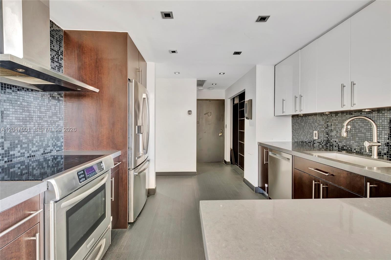 A modern kitchen features dark wood cabinetry, white upper cabinets, stainless steel appliances, and tile backsplashes — 11111 Biscayne Blvd, Miami FL 33181, MIAMI, FL