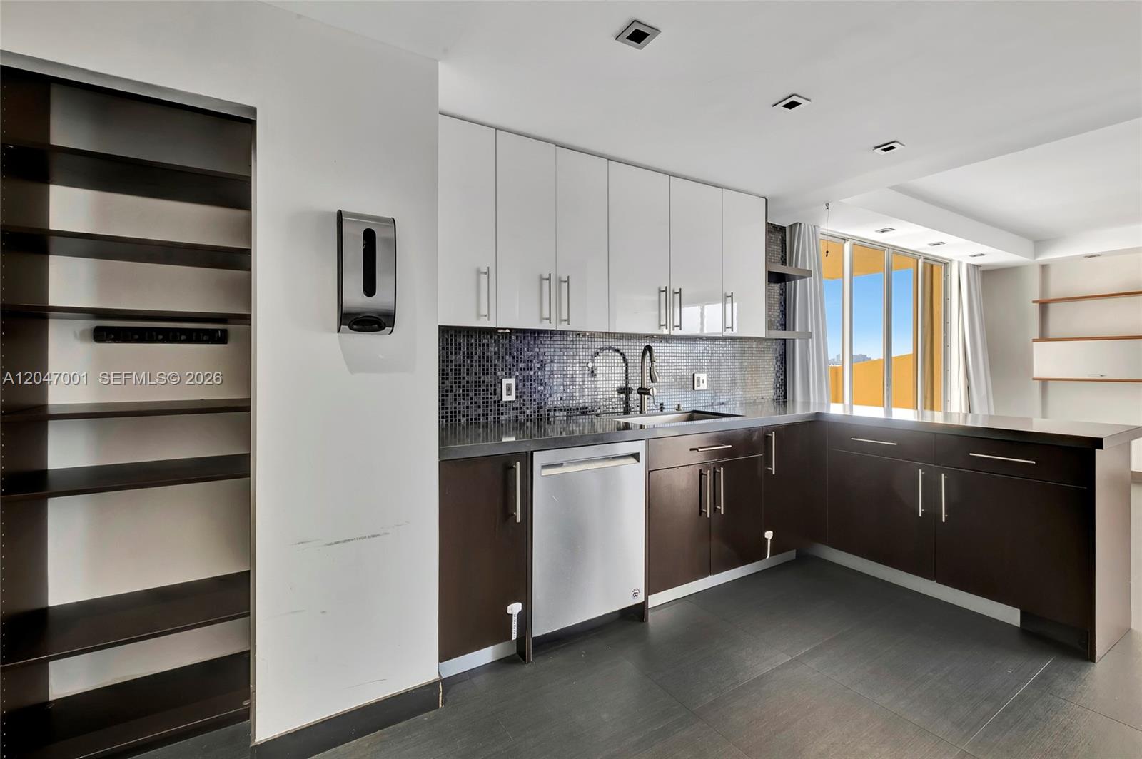 A kitchen features white upper cabinets, dark lower cabinets, a mosaic backsplash, and stainless appliances — 11111 Biscayne Blvd, Miami FL 33181, MIAMI, FL