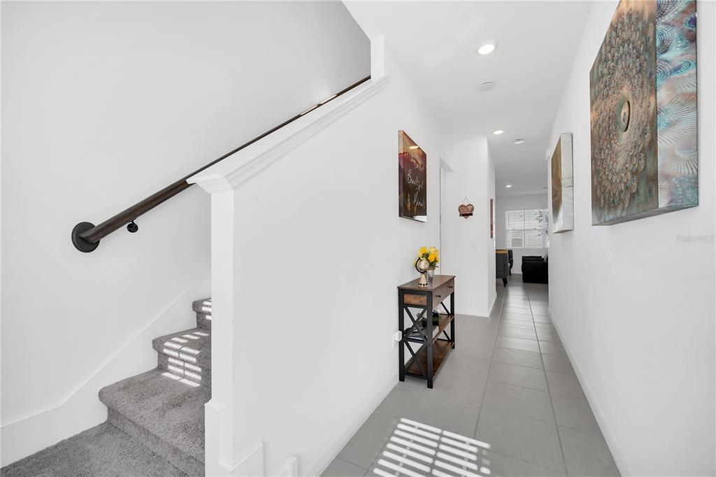 A hallway with gray tile flooring leads past a staircase with carpeted steps — 808 LONGBOAT DRIVE, DAVENPORT, FL