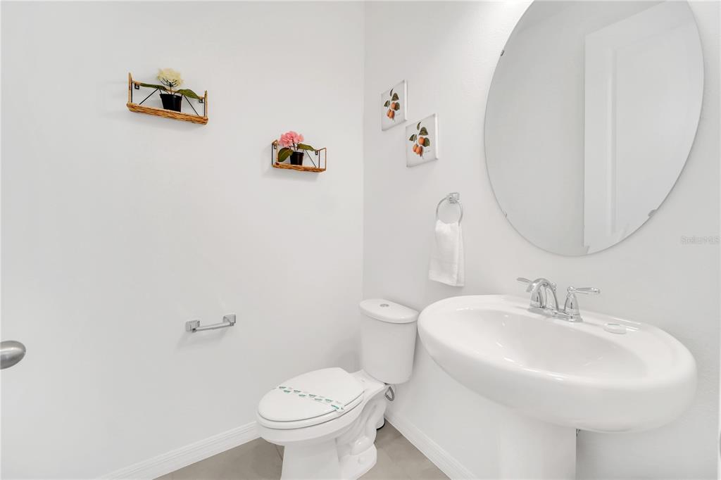 A white half bathroom features a pedestal sink, round mirror, and wall-mounted decorative shelves — 808 LONGBOAT DRIVE, DAVENPORT, FL