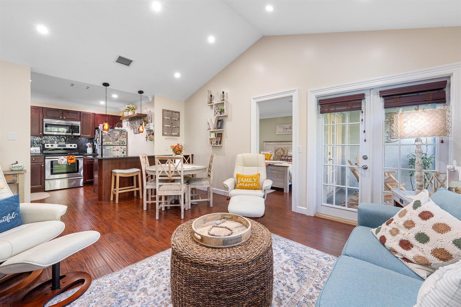 An open-concept living room and kitchen featuring hardwood floors, a vaulted ceiling, and patio doors — 1616 SE Green Acres Circle # M204, FL 34952, FL
