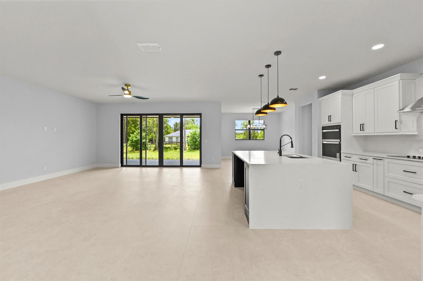 A bright open-concept kitchen and living area featuring white cabinetry, a large island, and sliding doors — 14826 89th Place N, Loxahatchee FL 33470, LOXAHATCHEE, FL