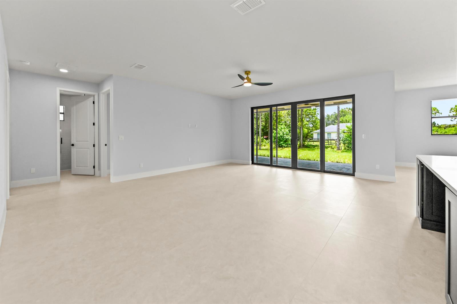 A spacious living room features light tile flooring, a ceiling fan, and large sliding glass doors — 14826 89th Place N, Loxahatchee FL 33470, LOXAHATCHEE, FL