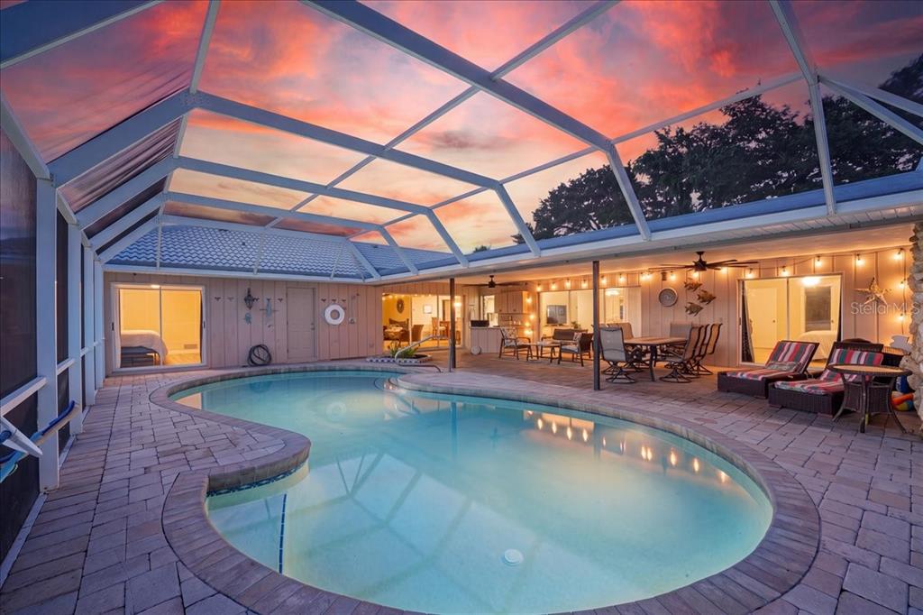 A screened-in patio features a kidney-shaped swimming pool, paver decking, and outdoor dining furniture — 413 SIGNORELLI DRIVE, NOKOMIS, FL