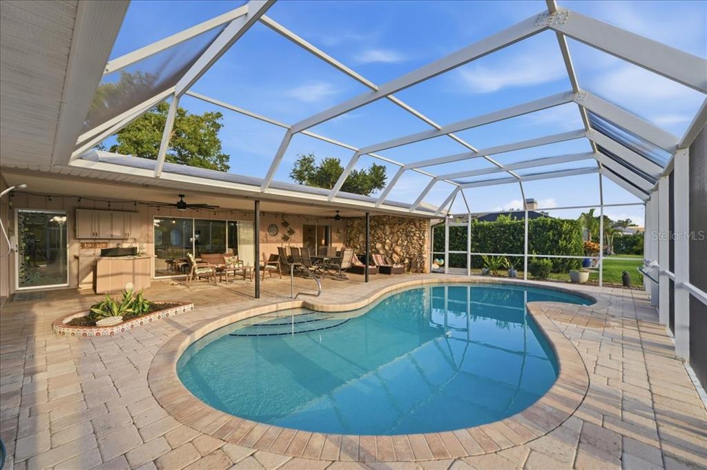 A screened-in patio features a kidney-shaped swimming pool, stone wall, and paver deck — 413 SIGNORELLI DRIVE, NOKOMIS, FL