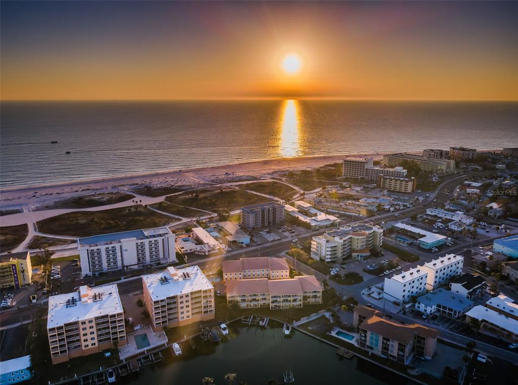An aerial view of a coastal town with multi-story buildings, a beach, and a sunset — 11595 GULF BOULEVARD UNIT 6, TREASURE ISLAND, FL