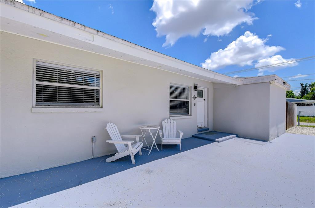 A white exterior wall features two windows, a doorway, and two chairs on a patio — 2714 E 98TH AVENUE, TAMPA, FL