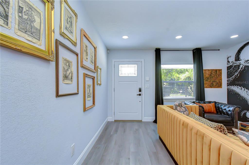 A living room features a yellow tufted sofa, framed wall art, and a white door — 2714 E 98TH AVENUE, TAMPA, FL