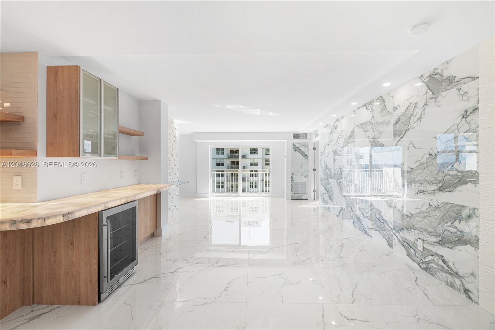 A modern room features white marble flooring, a marble accent wall, and a wood-toned kitchenette — 4505 S Ocean Blvd # 703, Highland Beach FL 33487, HIGHLAND BEACH, FL