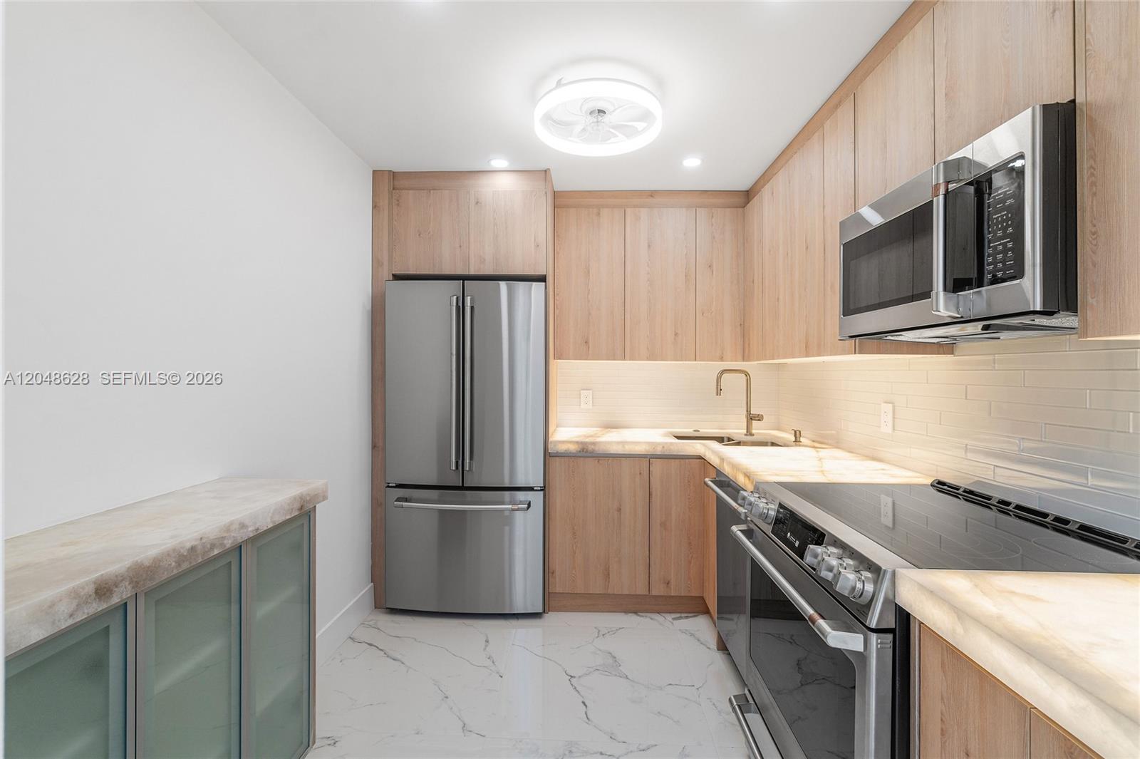 A modern kitchen features light wood cabinets, stainless steel appliances, and white marble-patterned flooring — 4505 S Ocean Blvd # 703, Highland Beach FL 33487, HIGHLAND BEACH, FL