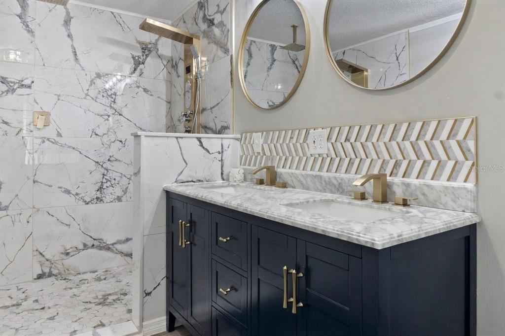 A bathroom features a double vanity with gold fixtures, marble countertops, and a walk-in shower — 6533 JACK STREET, PUNTA GORDA, FL