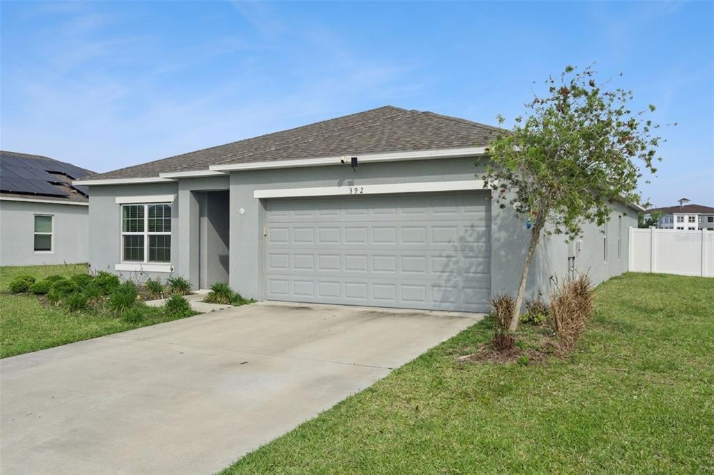 A single-story house with a gray stucco exterior, a two-car garage, and a concrete driveway — 392 CITRINE LOOP, KISSIMMEE, FL