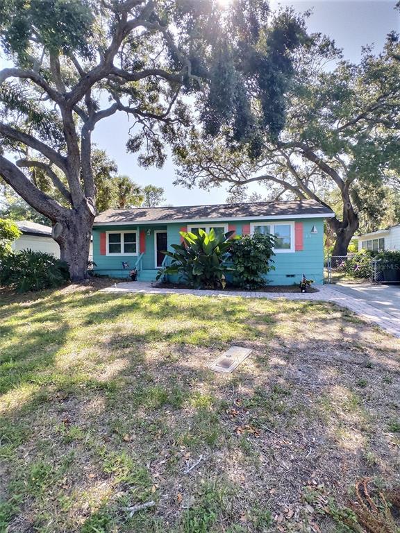 A teal, single-story house with white trim sits behind a large tree in a yard — 1431 PALOMA LANE, DUNEDIN, FL