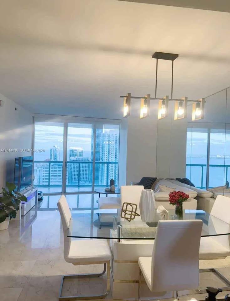 A dining area with a glass table and modern chandelier overlooks a city skyline view — 495 Brickell Ave # 4809, Miami FL 33131, MIAMI, FL