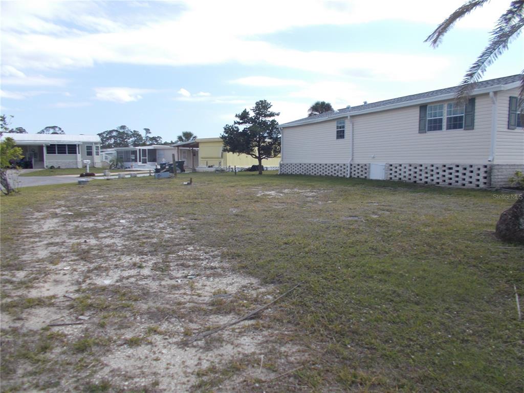 A grassy lot sits between a light-colored mobile home and neighboring residential properties — 5501 HOLIDAY PARK BOULEVARD, NORTH PORT, FL
