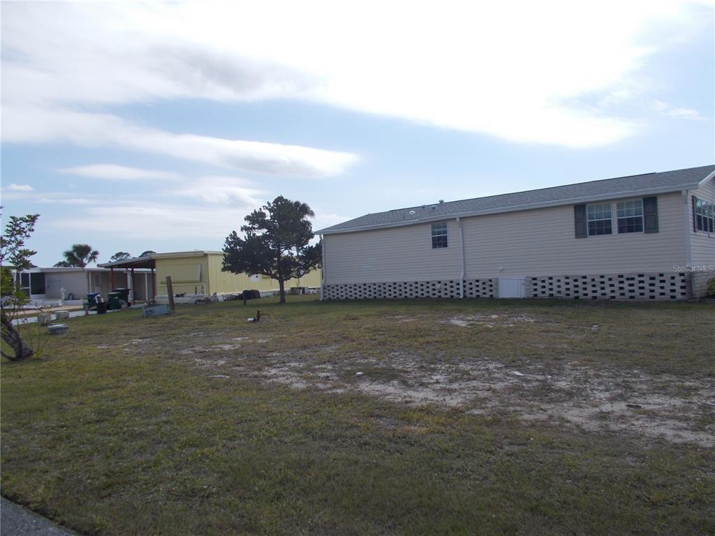 A side view of a light-colored manufactured home with a lattice foundation and a grassy yard — 5501 HOLIDAY PARK BOULEVARD, NORTH PORT, FL