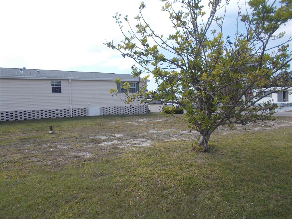 A side view of a light-colored mobile home with a lattice skirting and a tree — 5501 HOLIDAY PARK BOULEVARD, NORTH PORT, FL