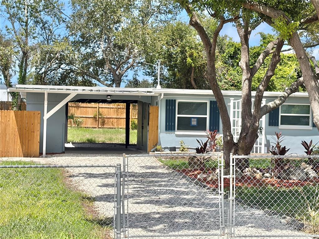 A light blue single-story house features a gravel driveway, a carport, and a chain-link fence — 12119 VICTORY DRIVE, HUDSON, FL