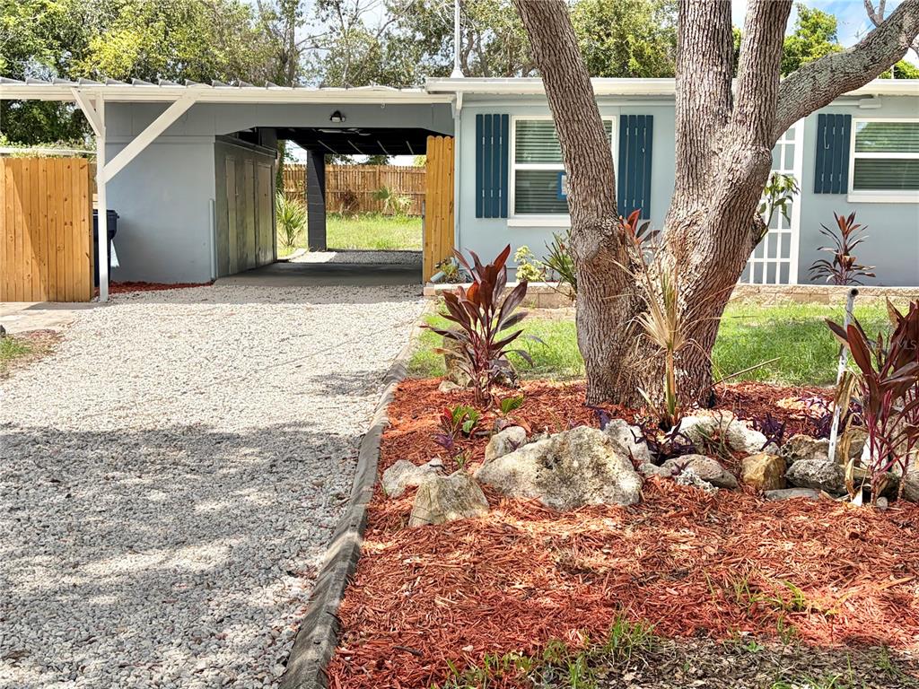 A gravel driveway leads to a carport beside a light blue house with red mulch — 12119 VICTORY DRIVE, HUDSON, FL