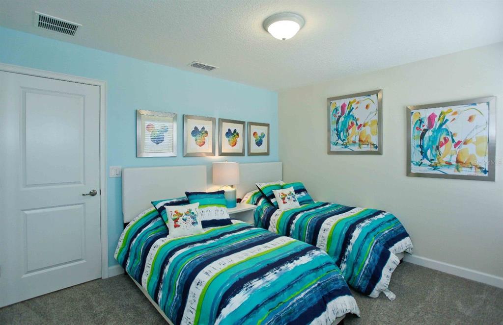 A bedroom with two twin beds, blue-striped bedding, and colorful Mickey Mouse wall art — 4839 KINGS CASTLE CIRCLE, KISSIMMEE, FL