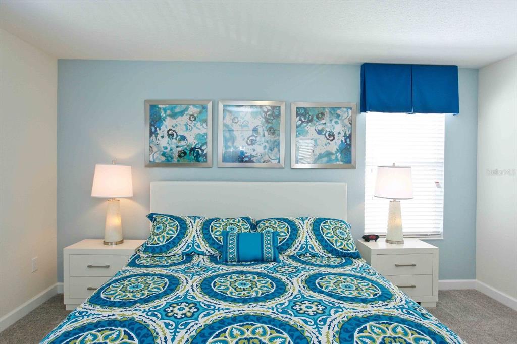 A bedroom features a bed with a blue patterned comforter, two nightstands, and wall art — 4839 KINGS CASTLE CIRCLE, KISSIMMEE, FL