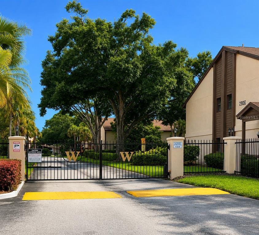 A gated entrance with a large tree and a multi-story building on the right — 3236 S SEMORAN BOULEVARD UNIT 15, ORLANDO, FL