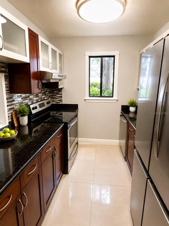 A galley kitchen features dark wood cabinets, black granite countertops, stainless steel appliances, and tile flooring — 3236 S SEMORAN BOULEVARD UNIT 15, ORLANDO, FL