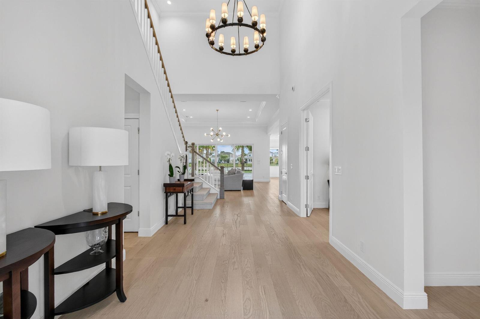 A bright, high-ceilinged foyer features light wood flooring, a grand chandelier, and a staircase — 9249 Crestview Circle, Palm Beach Gardens FL 33412, PALM BEACH GARDENS, FL