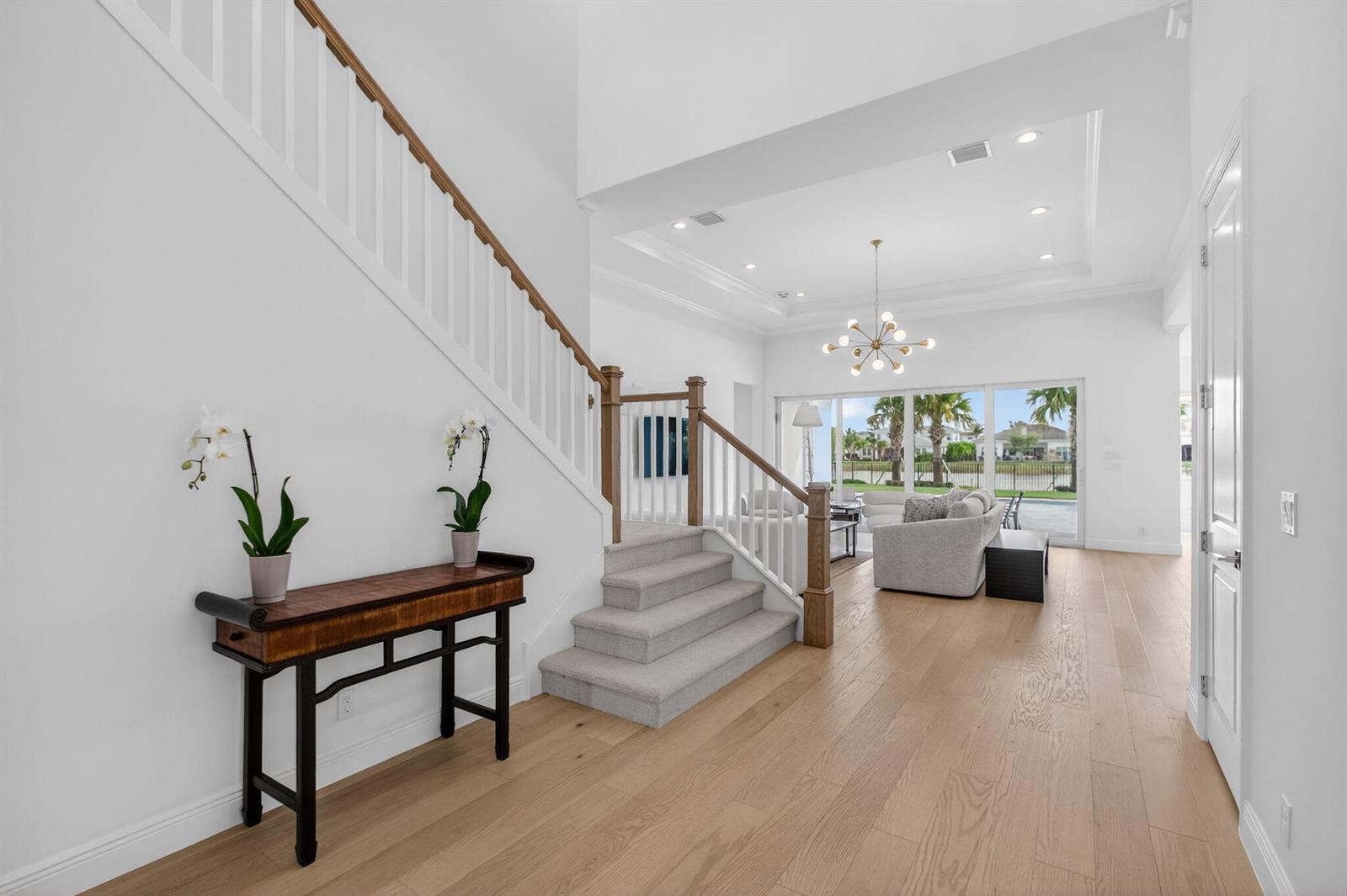 An entryway with light wood floors, a carpeted staircase, and a view into a living room — 9249 Crestview Circle, Palm Beach Gardens FL 33412, PALM BEACH GARDENS, FL