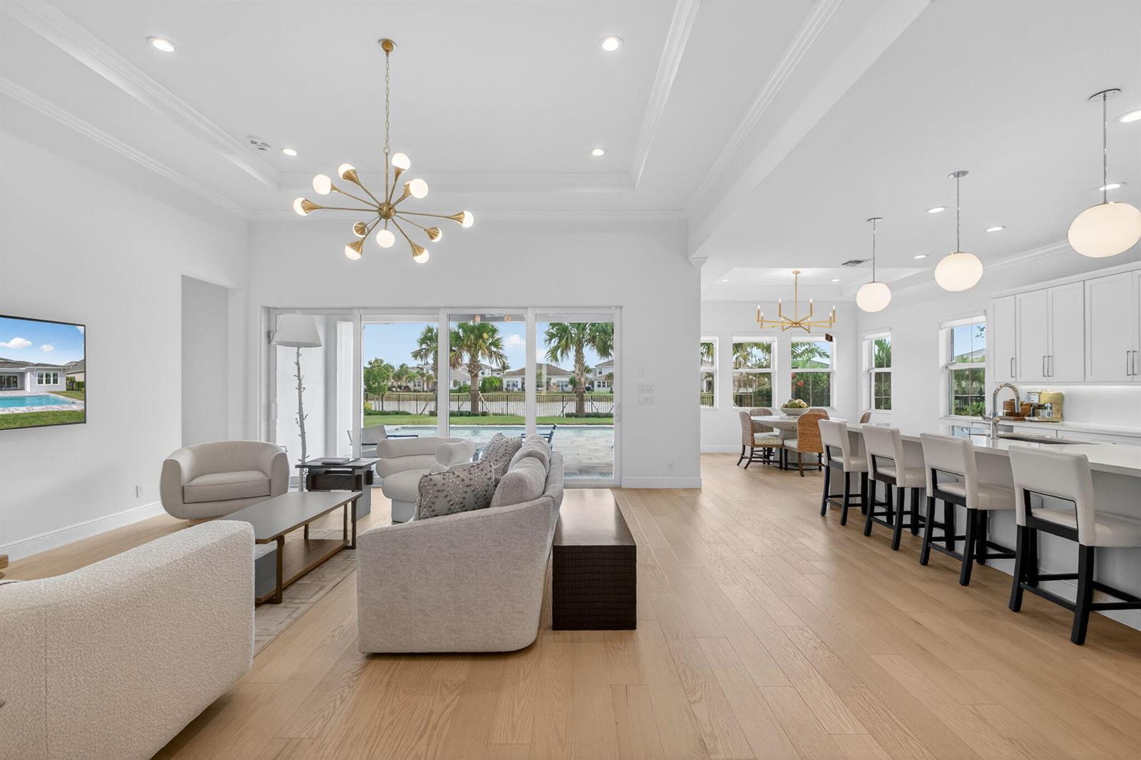A bright, open-concept living room and kitchen featuring light wood floors and large sliding doors — 9249 Crestview Circle, Palm Beach Gardens FL 33412, PALM BEACH GARDENS, FL