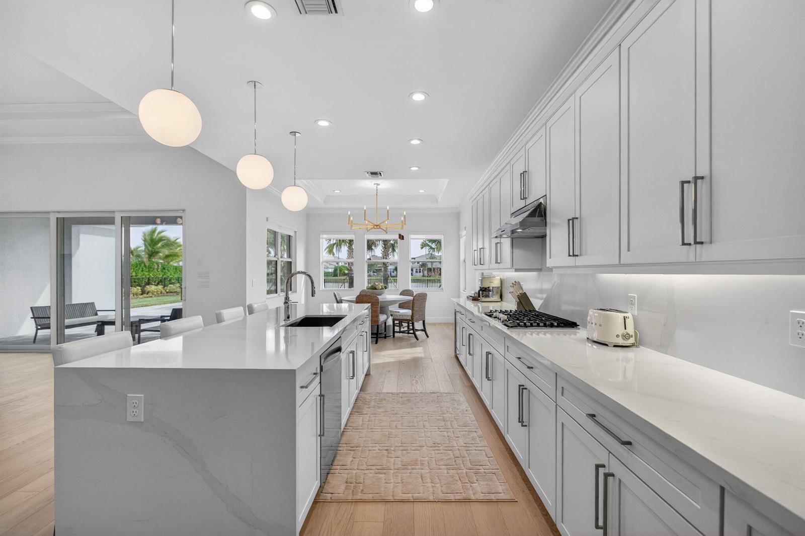 A modern white kitchen features a large quartz island, stainless steel appliances, and light wood flooring — 9249 Crestview Circle, Palm Beach Gardens FL 33412, PALM BEACH GARDENS, FL