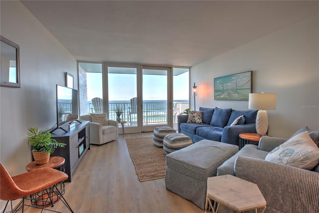 A living room features blue sofas, a television, and a balcony overlooking the ocean — 5203 S ATLANTIC AVENUE UNIT 815B, NEW SMYRNA BEACH, FL