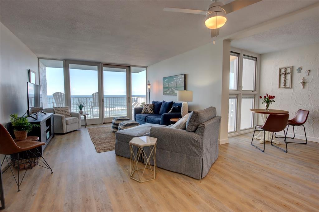 A living and dining area features light wood floors, blue furniture, and oceanfront balcony access — 5203 S ATLANTIC AVENUE UNIT 815B, NEW SMYRNA BEACH, FL