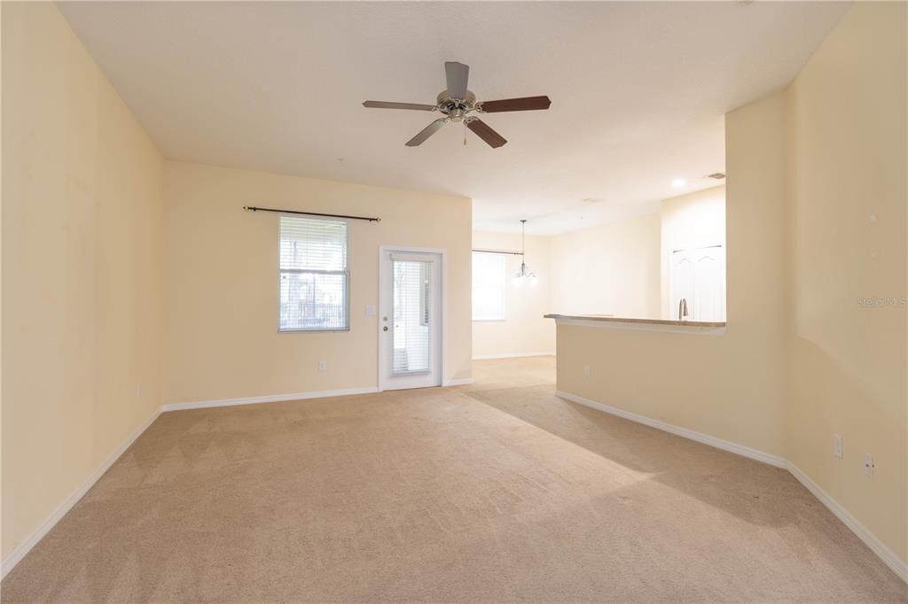 An empty living room features beige carpet, a ceiling fan, and a glass door — 15510 CAMPDEN STREET, WINTER GARDEN, FL