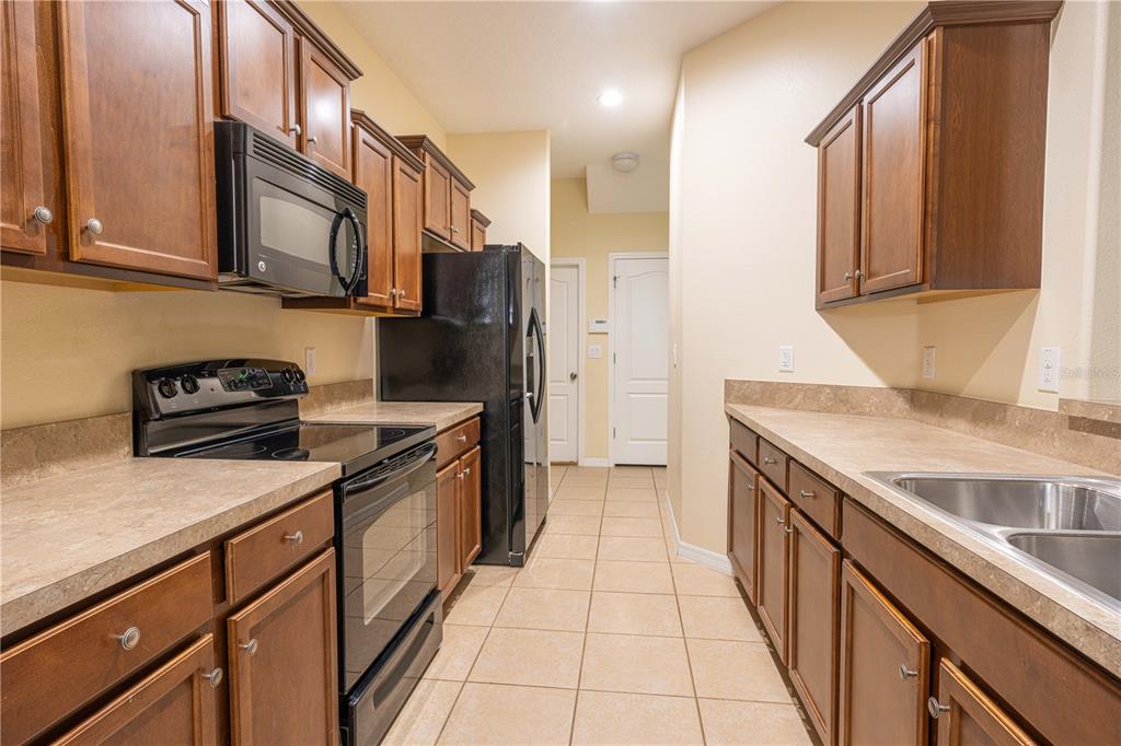 A galley kitchen features brown wood cabinets, black appliances, and tan laminate countertops — 15510 CAMPDEN STREET, WINTER GARDEN, FL