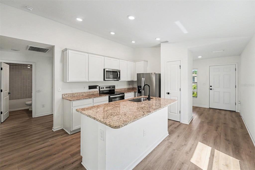 A kitchen with white cabinets, granite countertops, a center island, and wood-look flooring — 5669 FLOTILLA AVENUE, TAMPA, FL