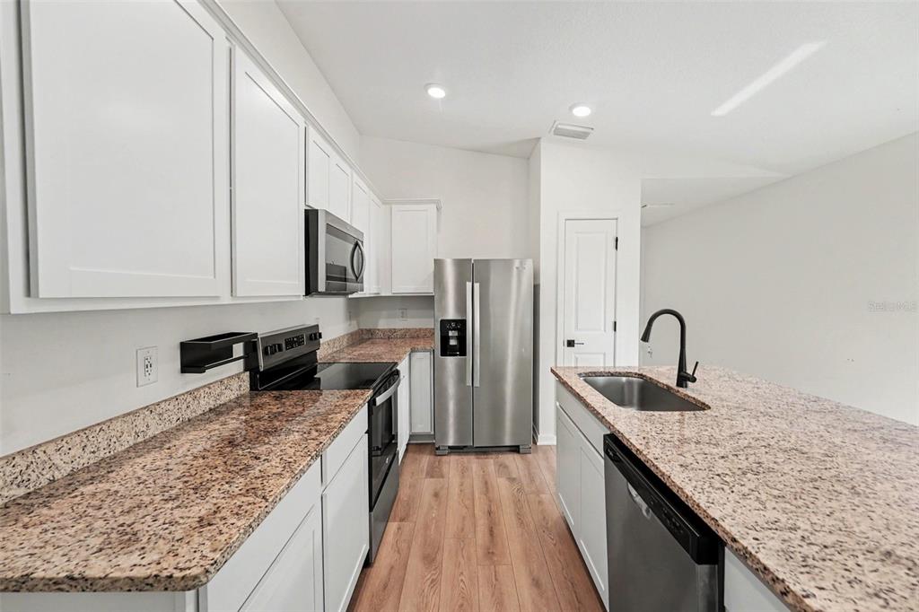 A kitchen features white cabinets, granite countertops, stainless steel appliances, and wood-look flooring — 5669 FLOTILLA AVENUE, TAMPA, FL