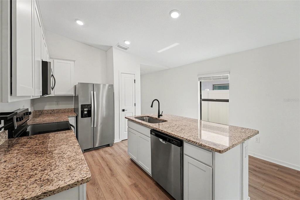 A kitchen features white cabinets, granite countertops, stainless steel appliances, and wood-look flooring — 5669 FLOTILLA AVENUE, TAMPA, FL